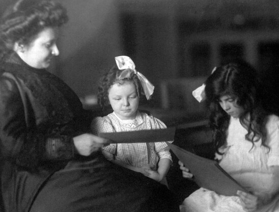 Zdjęcie przedstawia Marię Montessori siedzącą z dwoma dziewczynkami.